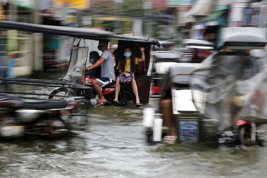 Residents ride motorcycles as they navigate a flooded road due to Typhoon Molave