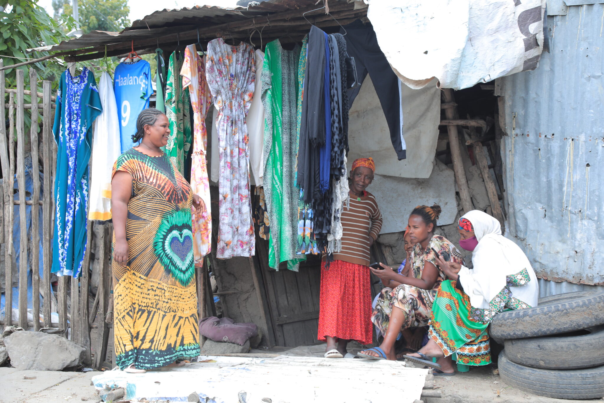 A smiling woman stands facing a groupof seated women, all wearing bright and colorful clothing.