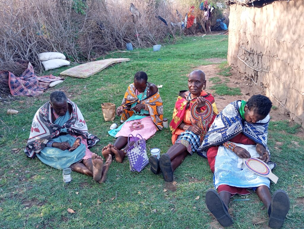 Tome alongside three women she's trained, sitting on the ground making their beaded jewelry.