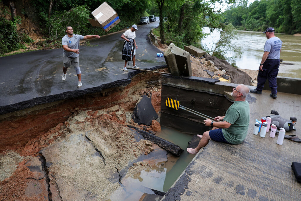 July 11, 2026, Lesterville, Missouri, USA: TREY MILLARD, left, of Columbia, Missouri, throws a box to his dad, ROB MILLARD, right, across a broken County Road 364 as his brother, KY MILLARD, prepares to hand off a baby carrier in Lesterville on Saturday. Flash flooding from the nearby Black River submerged the nearby campgrounds and eroded the road, stranding the Millards who spent the last week camping and [were] planning to leave the day the flooding came. 'There's people who lost a lot more,' Trey Millard said. (Credit Image: © Liz Rymarev/St. Louis Post-Dispatch via ZUMA Press Wire)